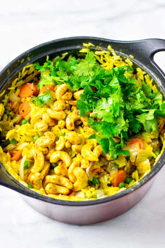 Fresh cilantro is used to garnish the Curried Rice in a large pot.