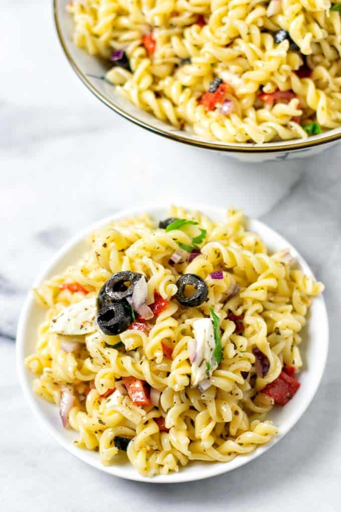 Closeup view of a portion of the Italian Pasta Salad on a small white plate with a serving bowl in the background.