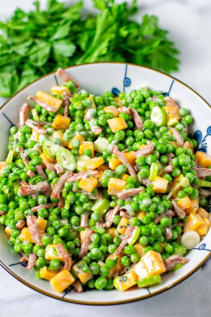Pea Salad in a large serving bowl with some fresh herbs in the background.