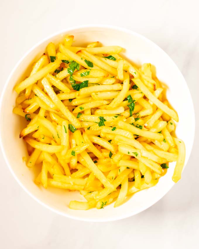 Top view on a white bowl with Garlic Fries garnished with parsley.