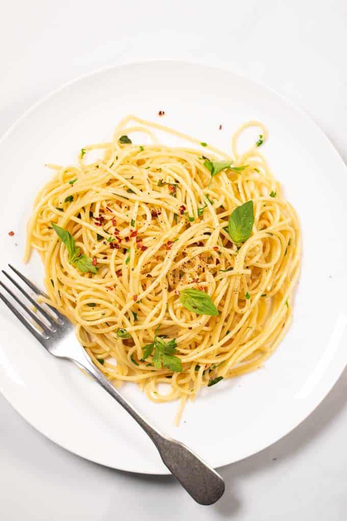 Top view on a portion of Garlic Pasta served on a white plate, with a silver fork.