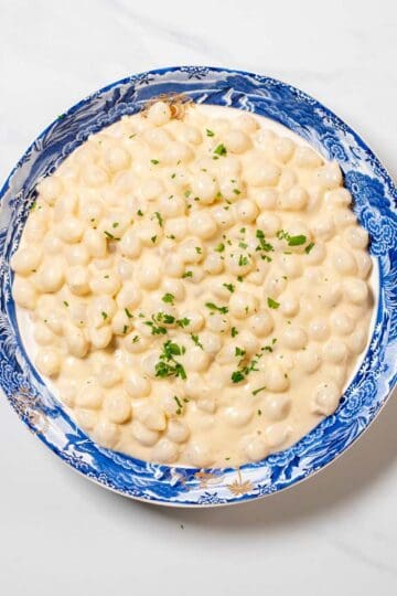 Top view on a serving bowl with Creamed Onions, garnished with fresh herbs.
