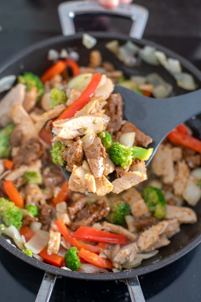 Closeup on a spoon of vegetables with chicken and steak.