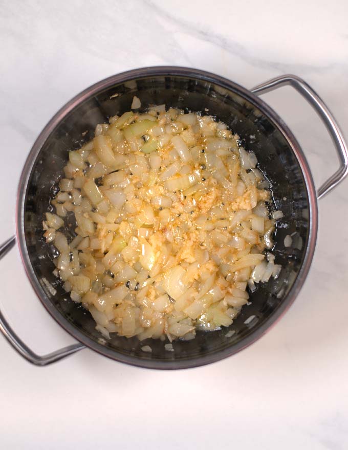 View of a large pot in which onions and garlic are sautéed.