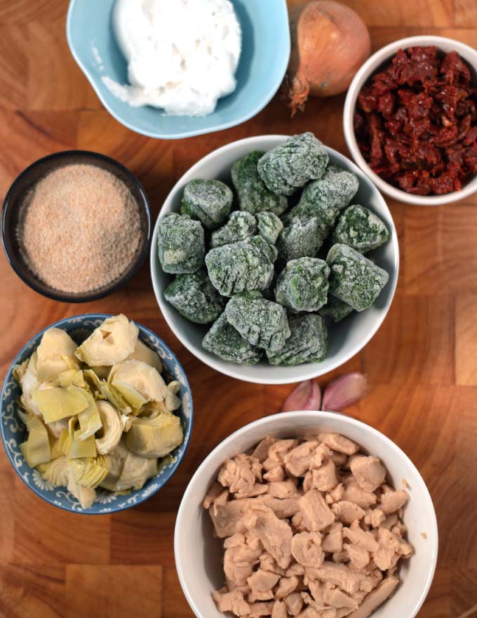 Ingredients needed to make Chicken Artichoke Casserole collected on a board.