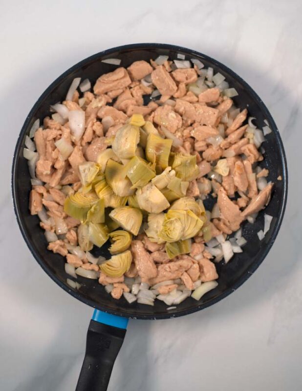 Onions, chicken, and artichokes are fried in a pan.