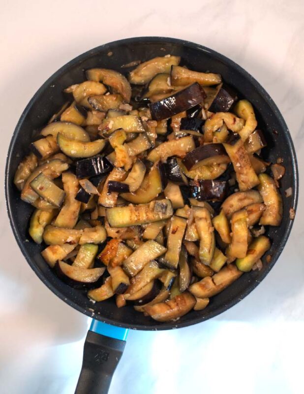 Sauteed onions and eggplant stripes in a large pan.