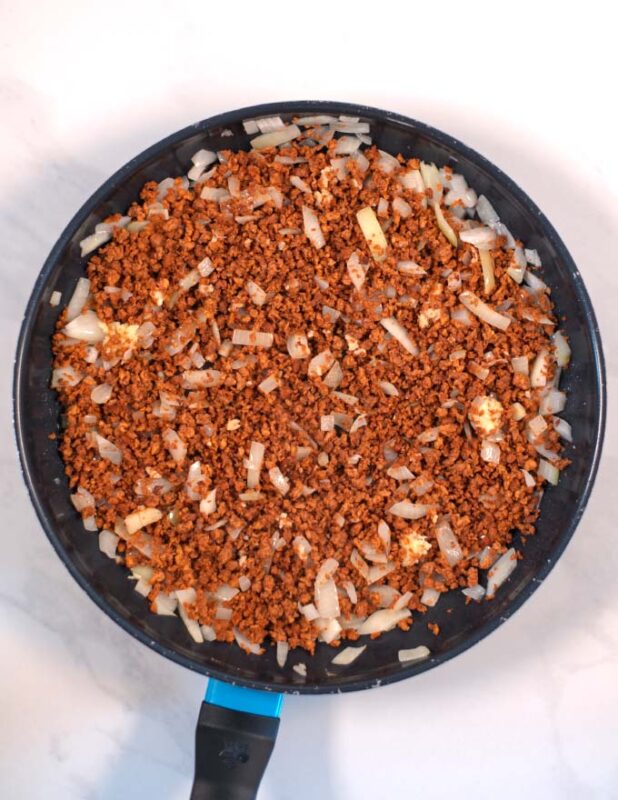 Vegan ground beef is added to the onions in the pan.