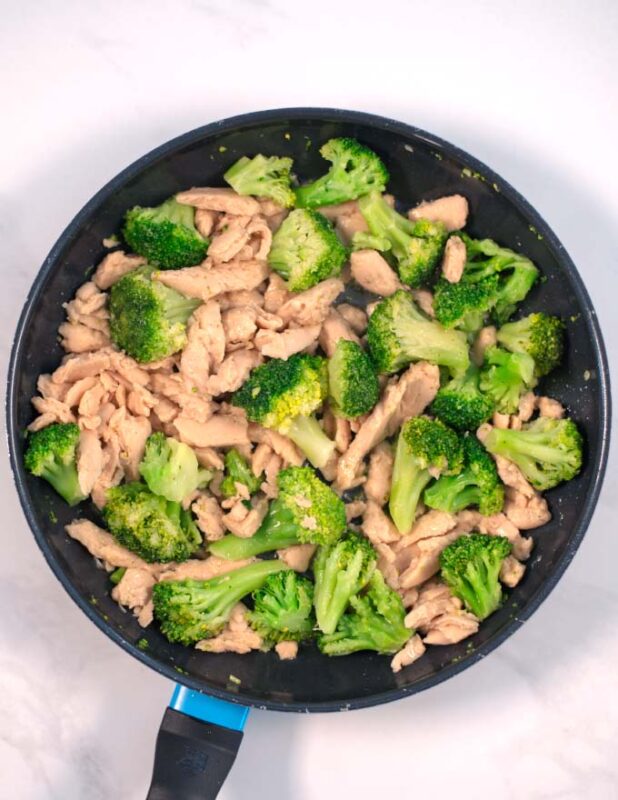 Vegan chicken and broccoli florets are cooked in a pan.