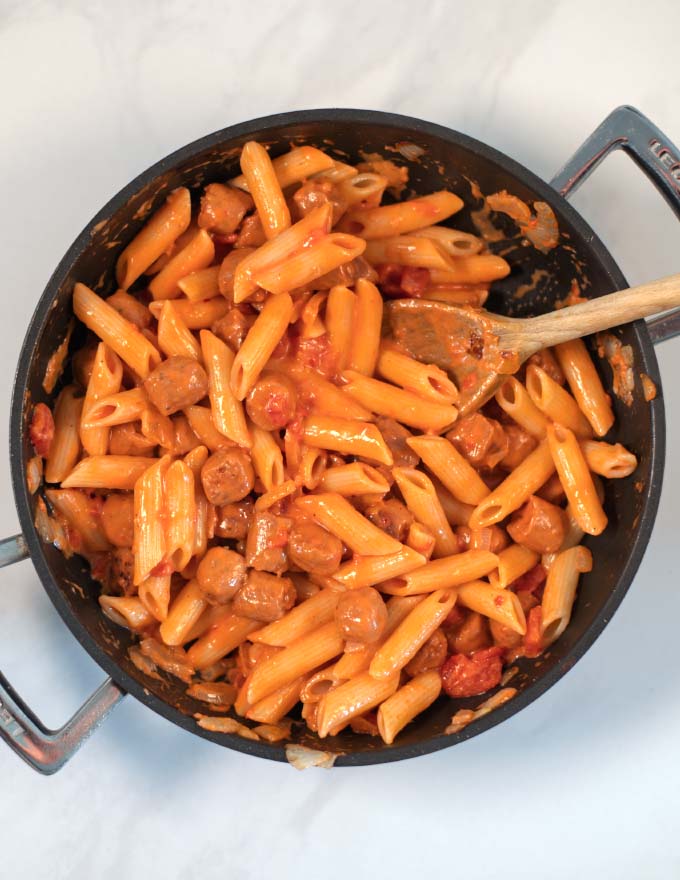Penne pasta is mixed with the sauce in the pan.