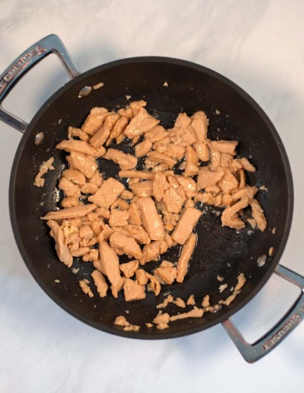 Vegan chicken and garlic are fried in a pan.