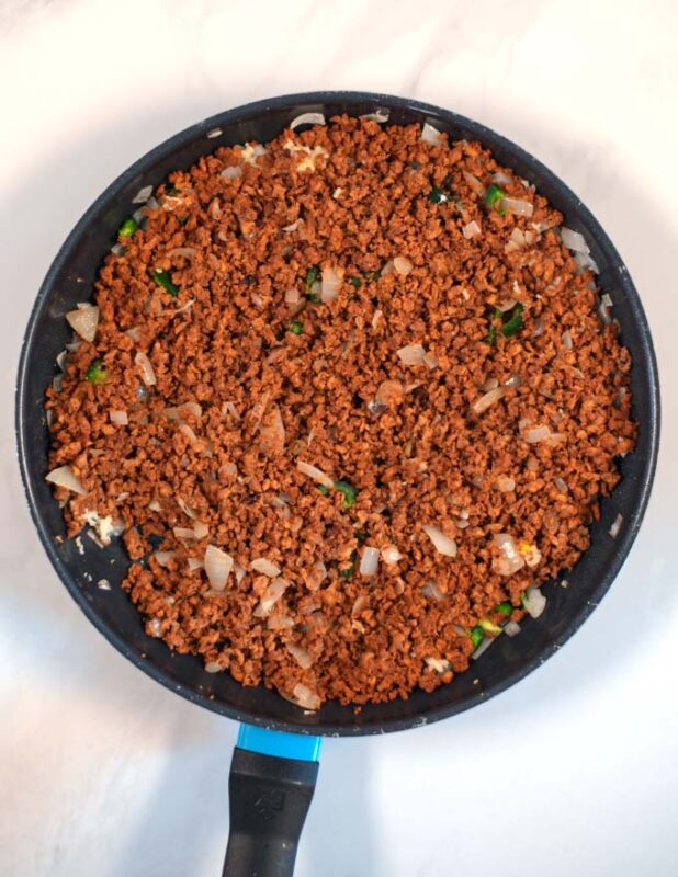 Veggie crumbles are fried in a pan with onions, garlic, and chilis.