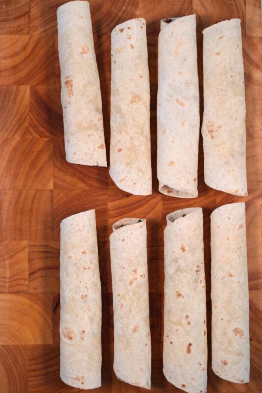 Ready rolled Flautas on a board.