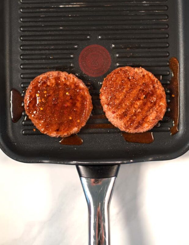 Burger patties are given with extra marinade in a grilling pan.