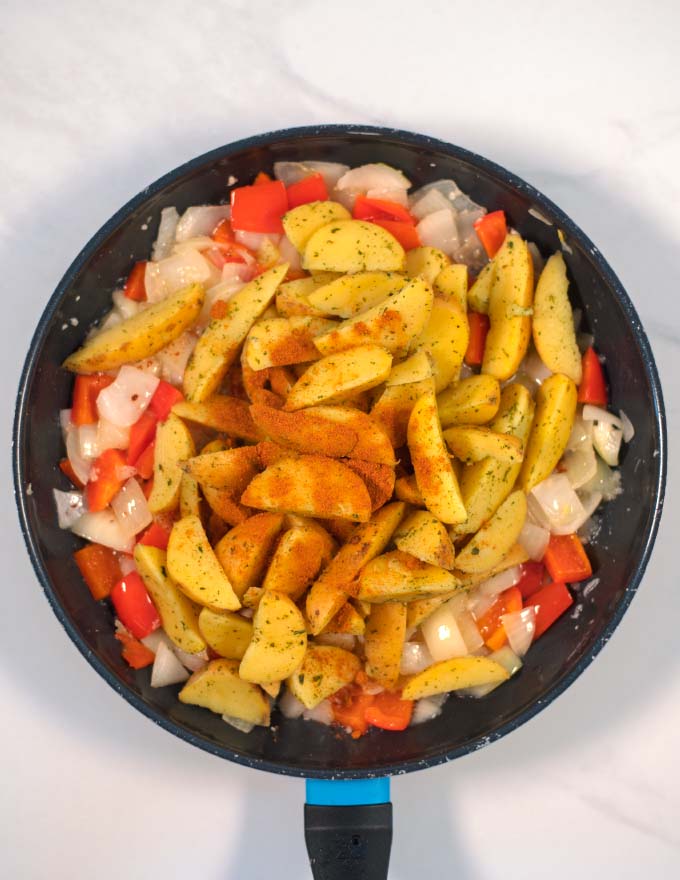 Potato wedges and spices are given to the pan with peppers and onions.