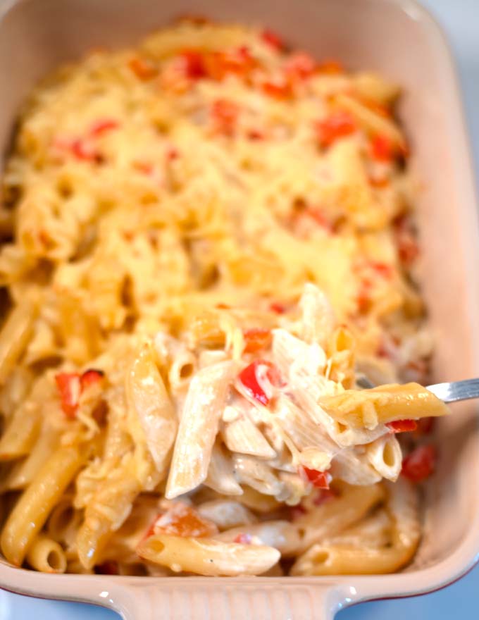A large spoon of Haitian Macaroni and Cheese is lifted out of the baking dish.