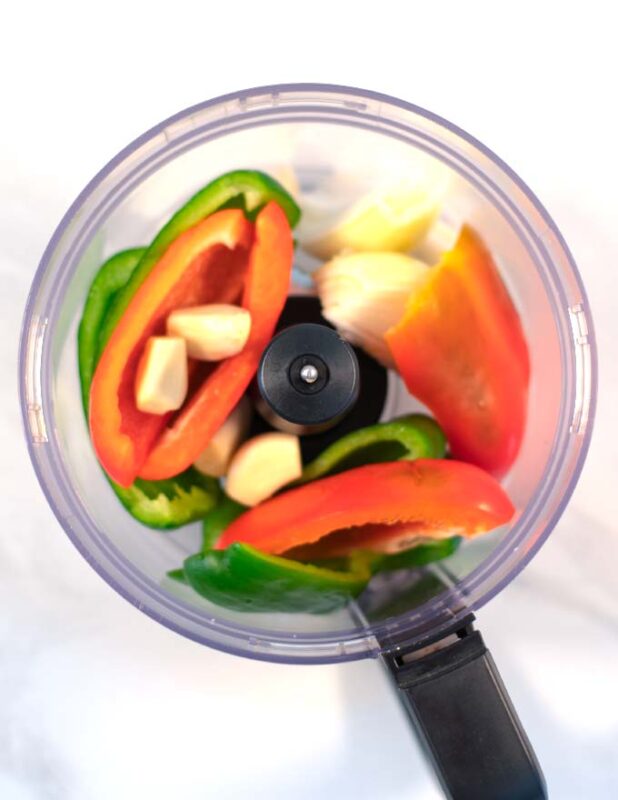 Peppers and garlic are added to the bowl of a food processor.