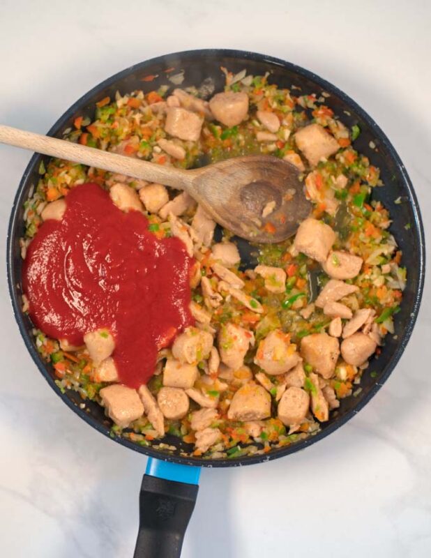 Pre-cooked vegan chicken bites and tomato sauce are mixed in the pan with Jambalaya mixture.