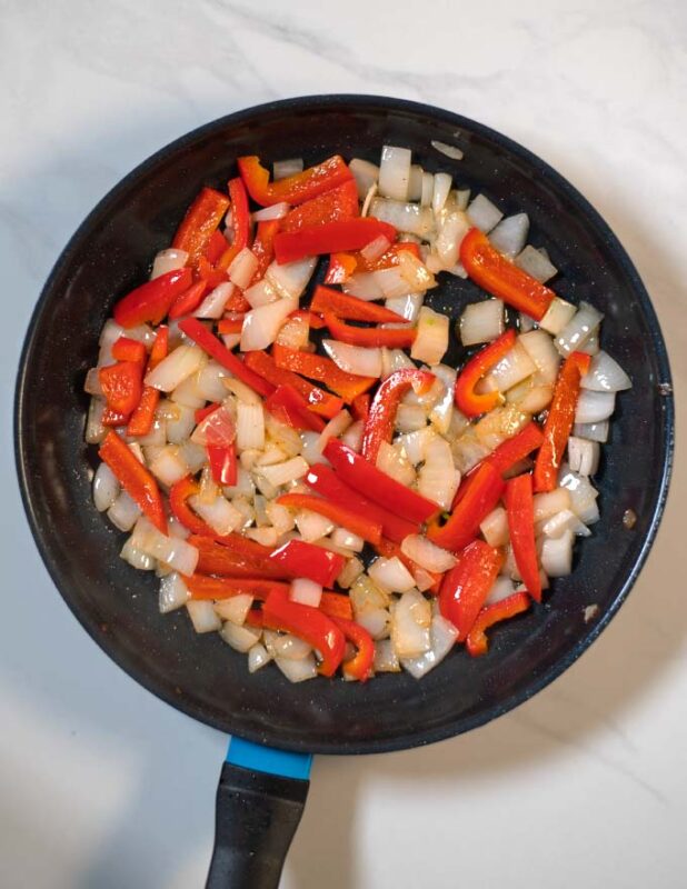 Pepper and onion are sauteed in a pan.