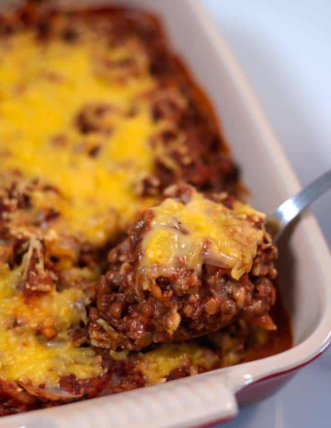 A spoonful of Lentil Casserole is lifted from the baking dish.