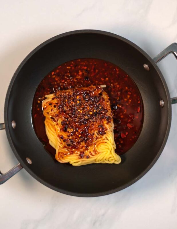 Noodles and sauce are prepared in a pan.