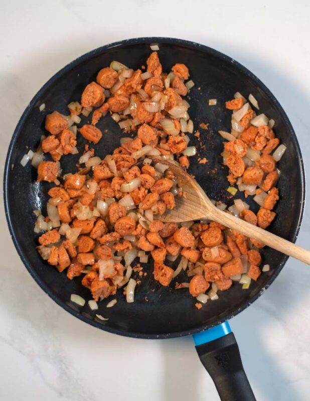 Vegan sausage crumbles and onions are sauteed in a pan.
