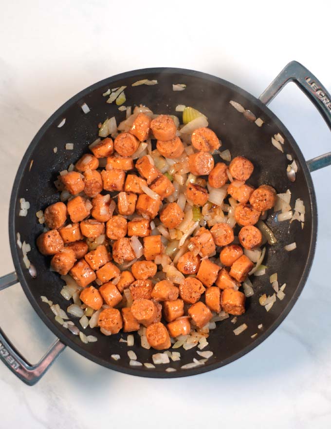Vegan sausage and onions are fried in a pan.
