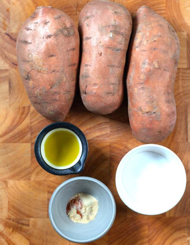 Ingredients needded to make Sweet Potato Fries are collected on a wooden board.