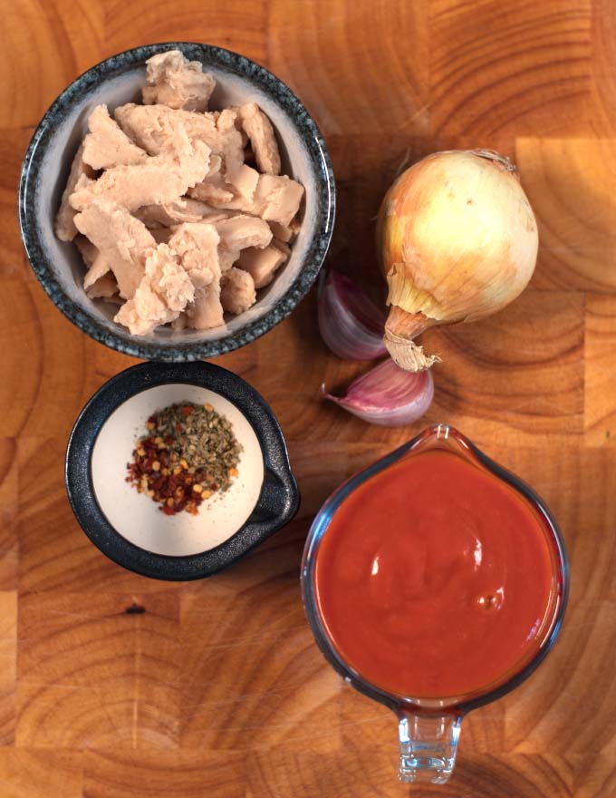 Ingredients needed to make Chicken Marinara Sauce are collected on a board.