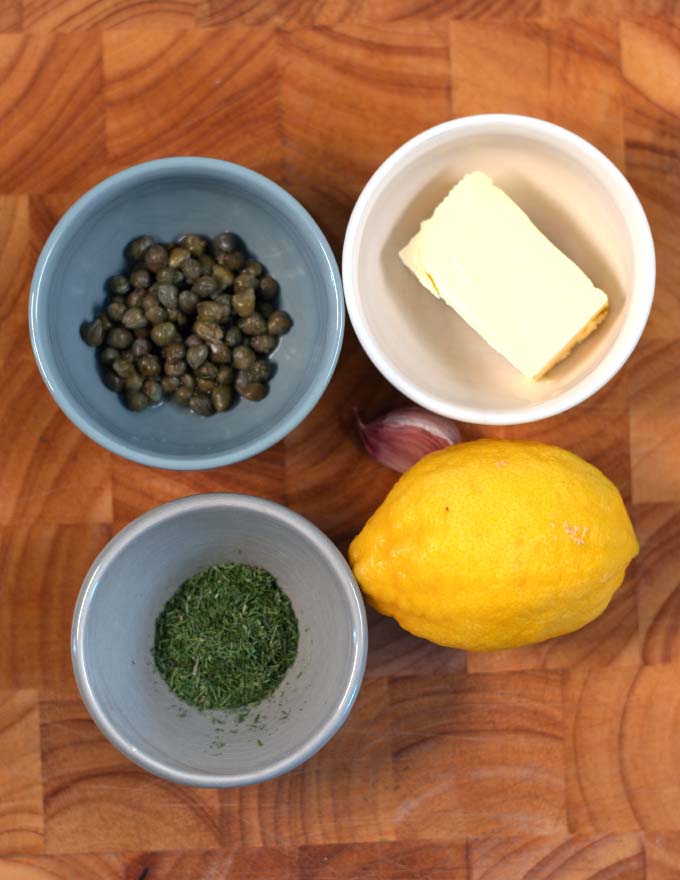 Ingredients needed to make Lemon Caper Sauce are collected on a wooden board.