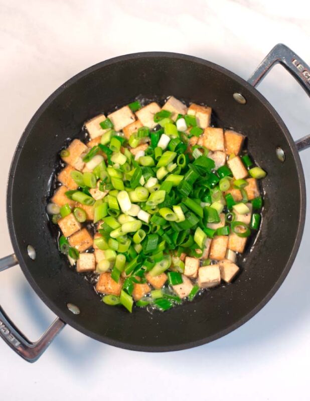 Tofu cubes are fried in oil with scallions.