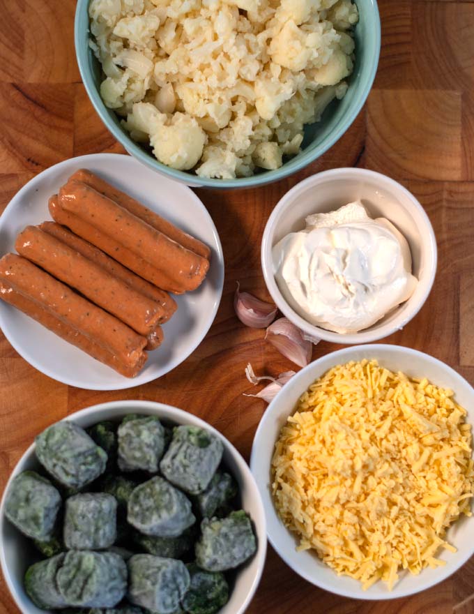 Ingredients needed to make low carb Cauliflower Sausage Casserole are collected on a wooden board.