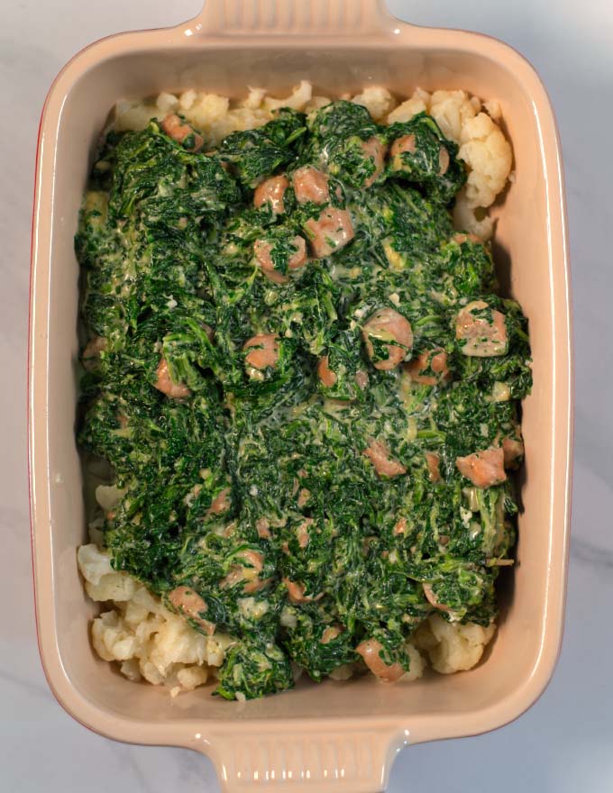 A baking dish with spinach and sausage mixture layered on top of cauliflower.