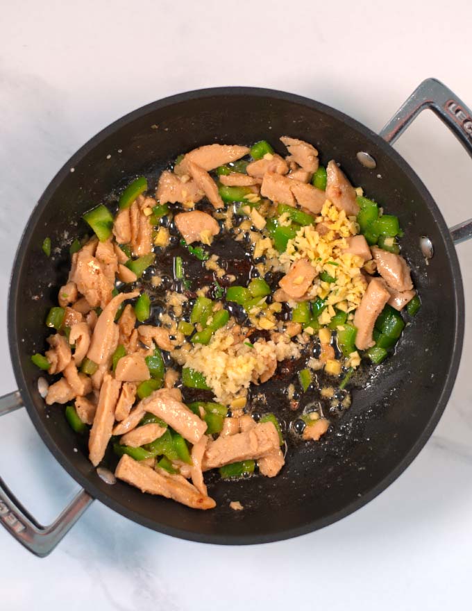 Vegan chicken, green bell pepper is fried in a pan with ginger and garlic.
