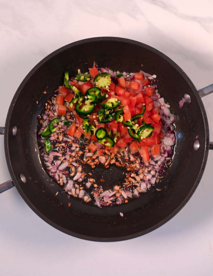 Red onions, tomato and jalapeno are sauteed in a pan.