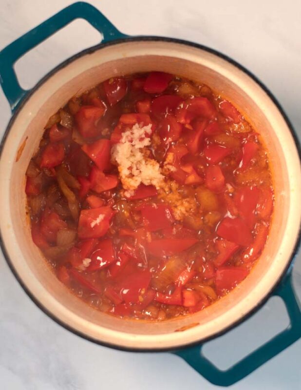 Onions and tomatoes are sauteed in a pot.