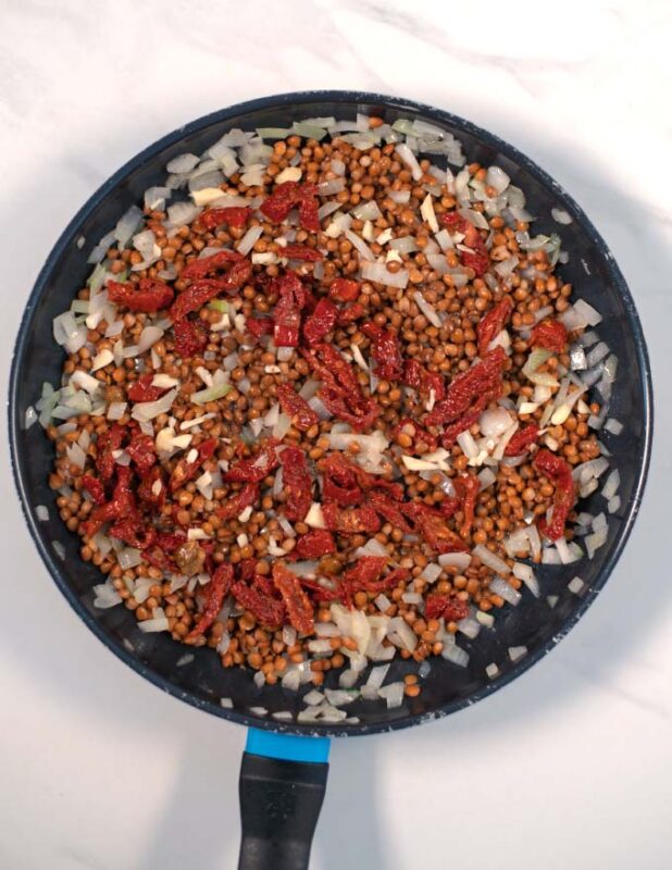 Onions, lentils, sundried tomatoes are sauteed in a pan.