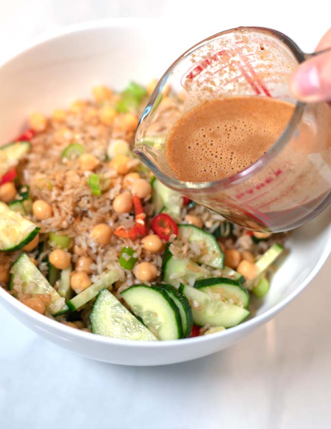 A small jar with the dressing is held over the Crispy Rice Salad.