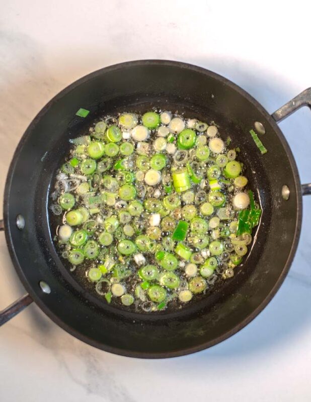 Scallions are fried in a pan.