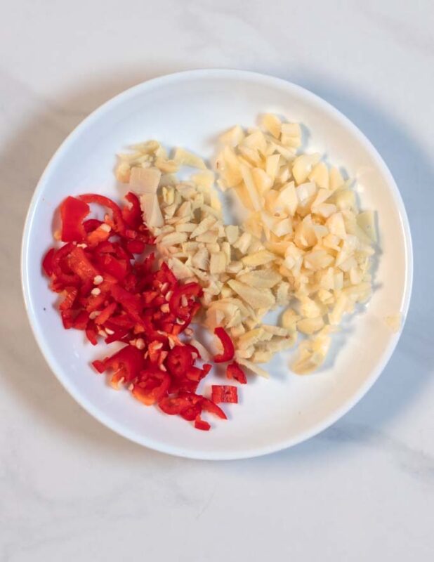 Finely chopped ginger, chili, and garlic on a white plate.