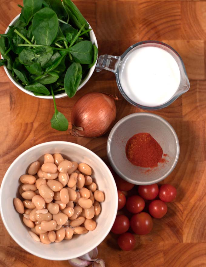 Ingredients needed to make Marry Me Butter Beans on a wooden cutting board.