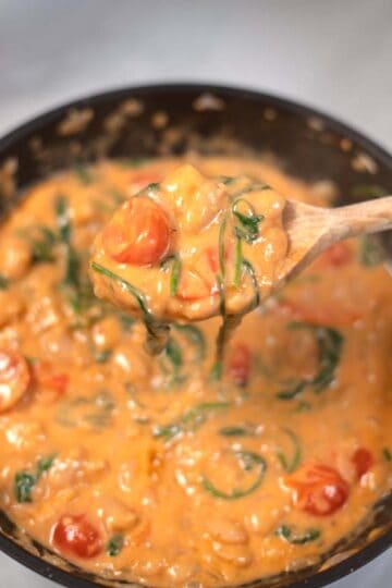 A large spoon lifts Marry Me Butter Beans from a pan.