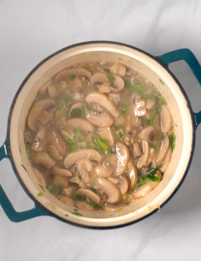 Mushrooms and scallions are fried in a large pot.