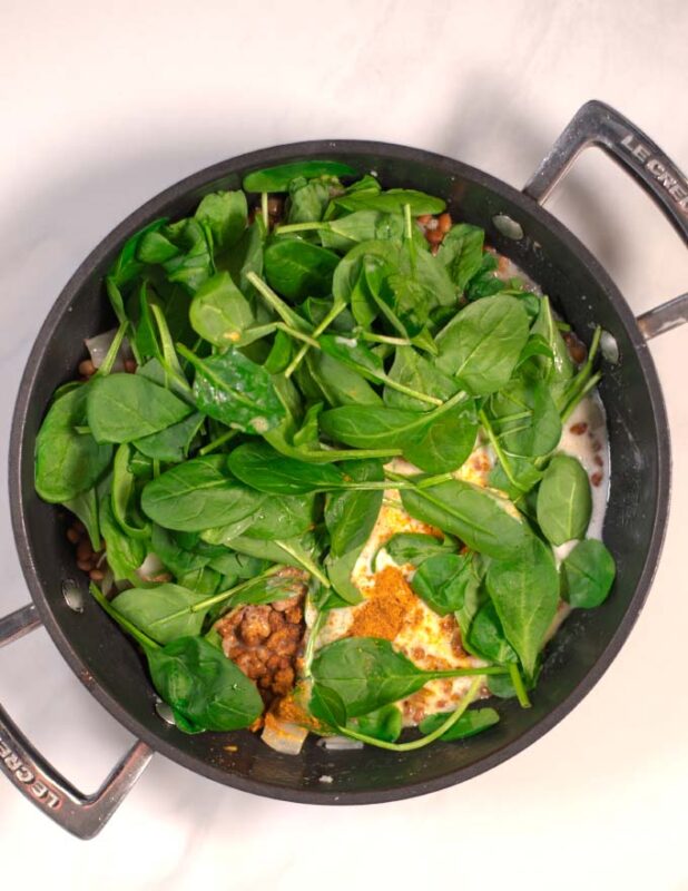 Spinach, spices, and cocunut milk are added to the pan with onions and lentils.