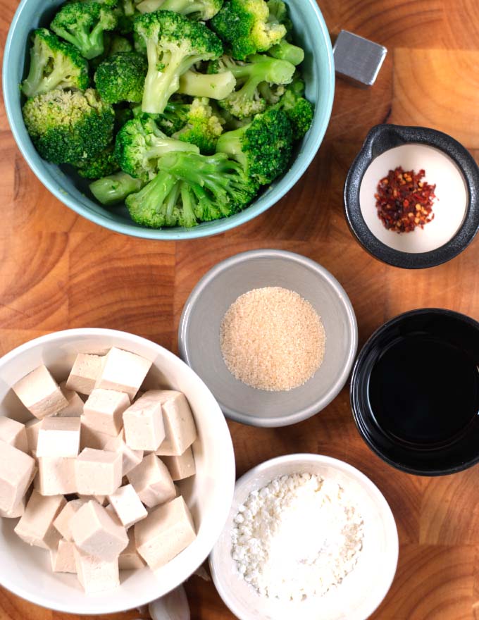 Ingredients needed to make Tofu and Broccoli collected on a wooden board.
